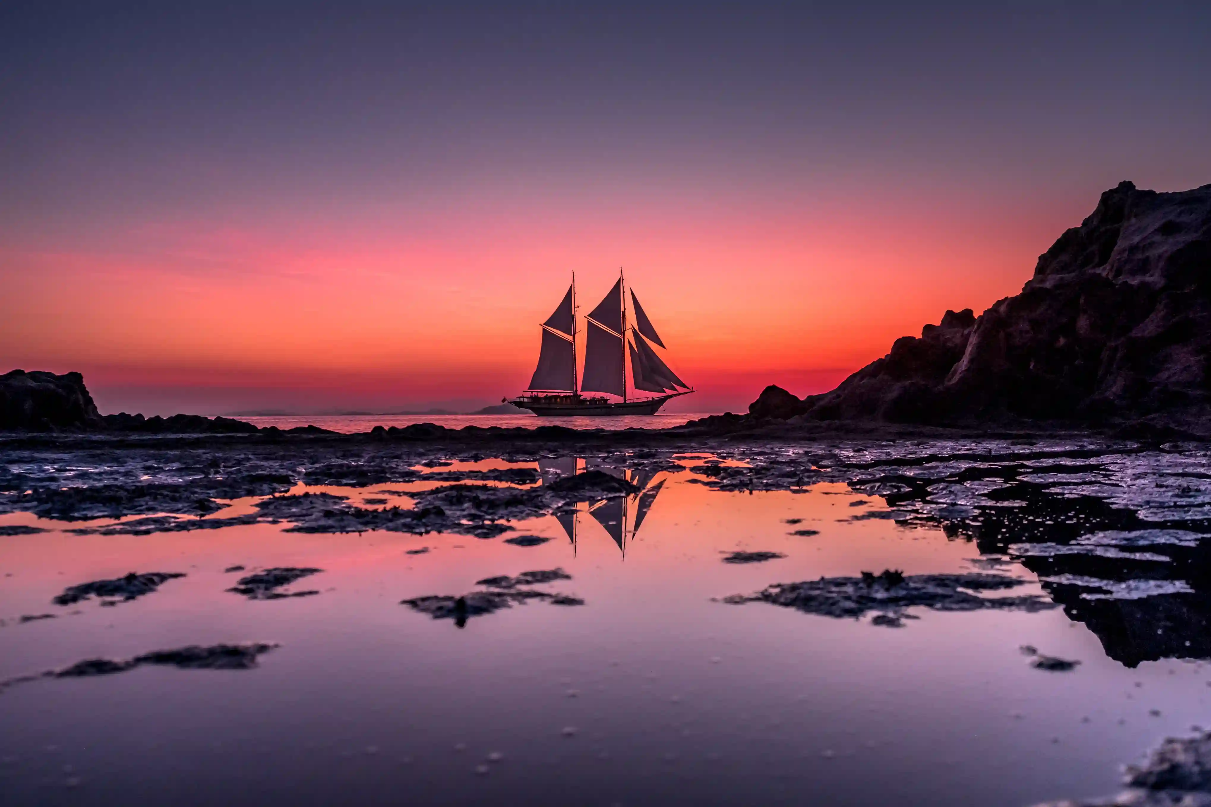 A phinisi silhouetted against a deep pink Komodo sunset