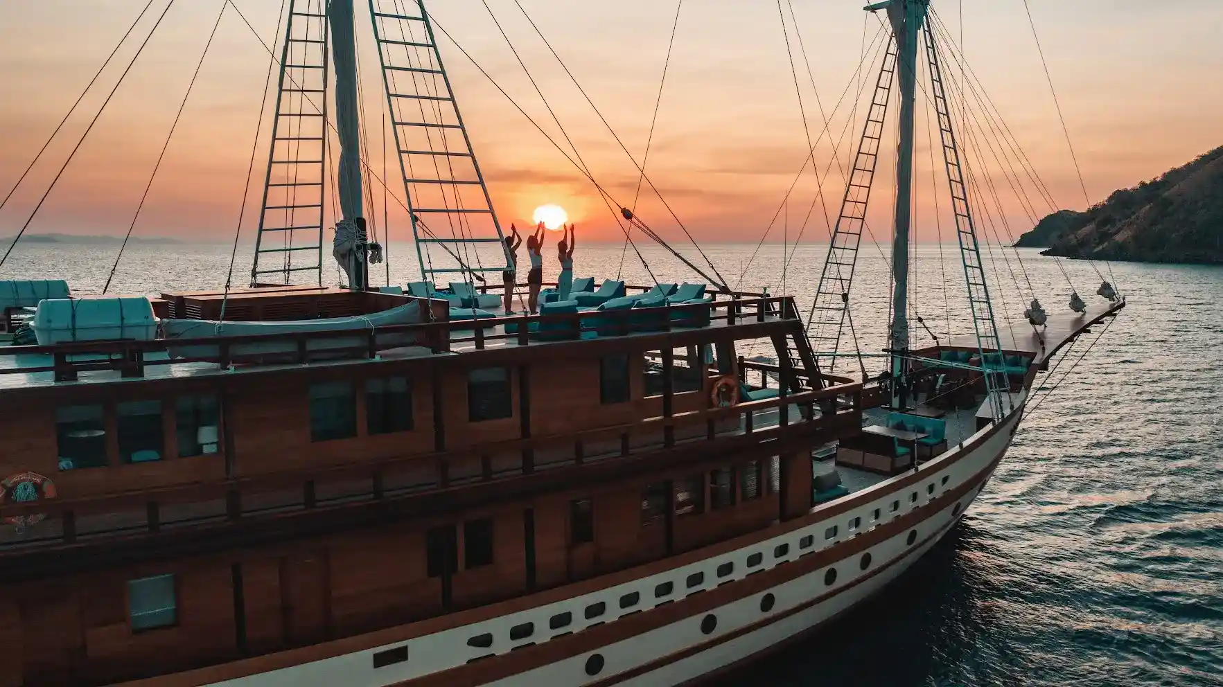 Guests practising yoga on the upper deck of a phinisi at sunset in Komodo National Park